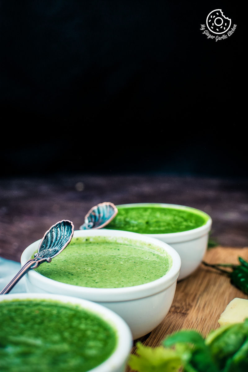 there are three bowls of green coriander chutney on a wooden table