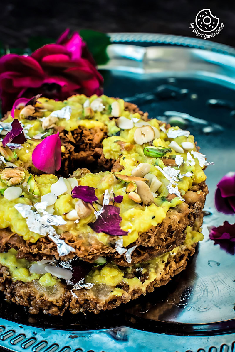 there is a stack of rajasthani malai ghevar with nuts and flowers on a plate
