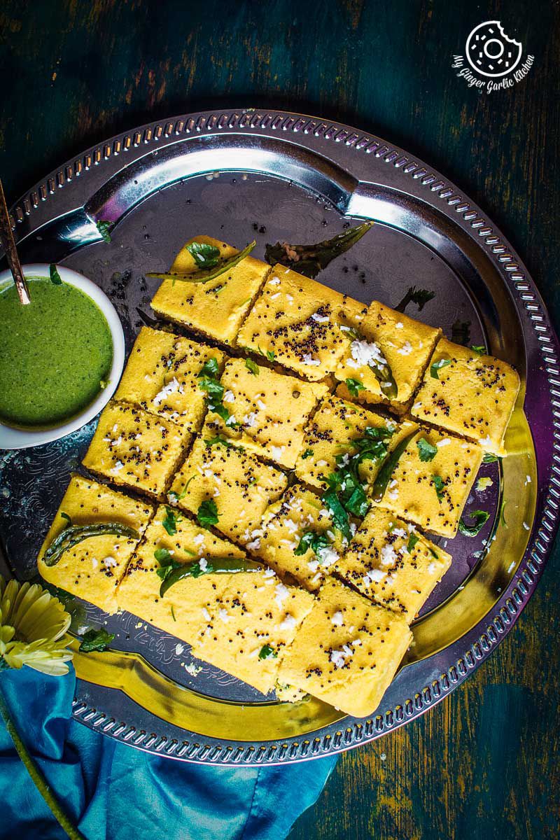 a plate of khaman dhokla with a bowl of green cilantro chutney