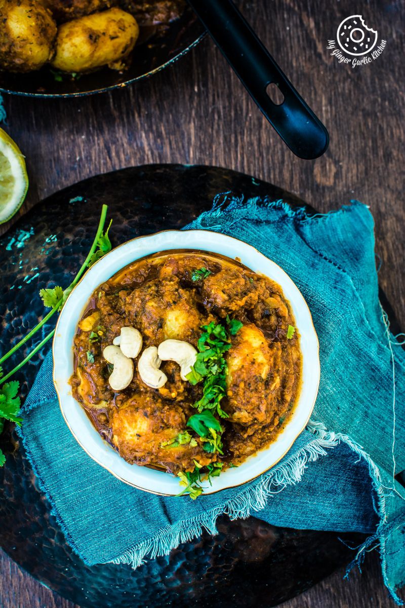 a bowl of lehsuni dum aloo with cashews and coriander leaves on a plate