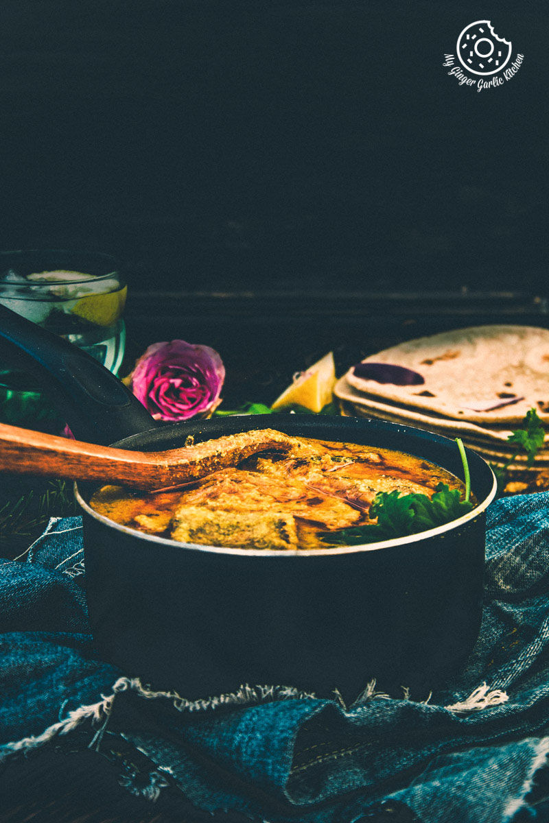 a pan of besan ke cheele ki sabzi on a table with a wooden spoon on a table with a blue cloth