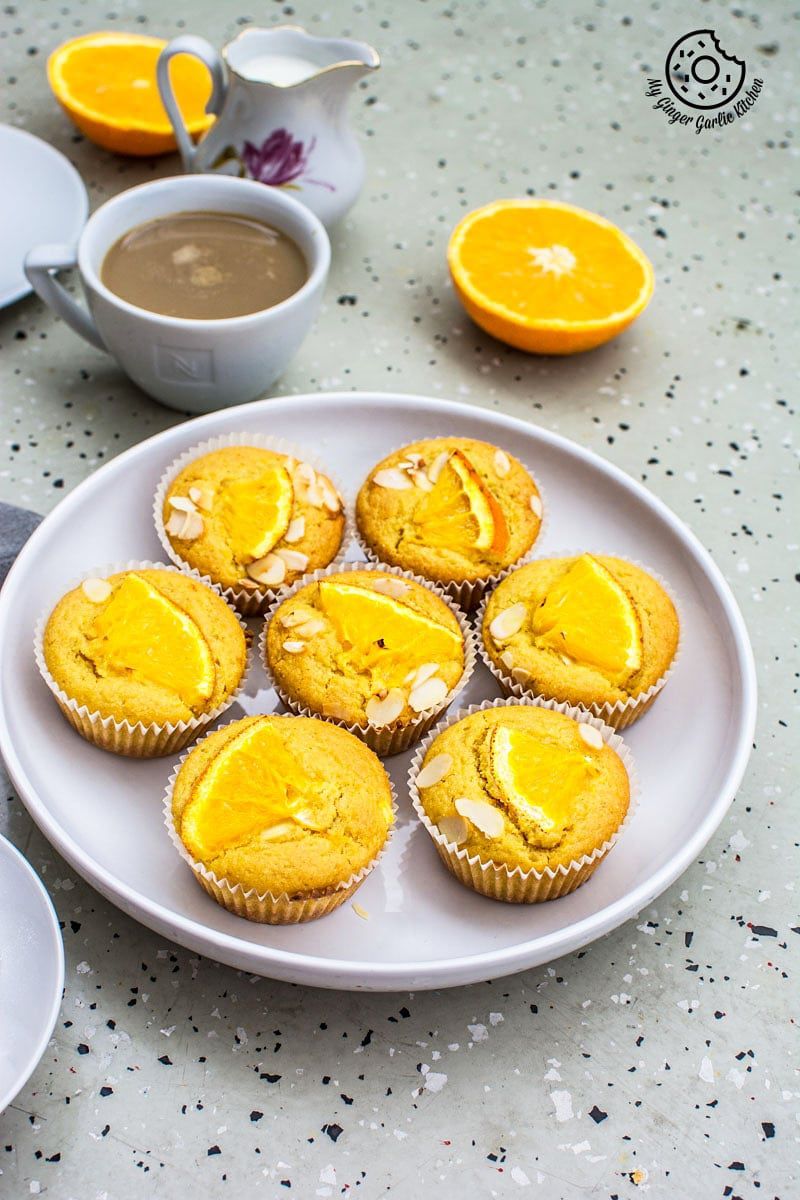 oranges and eggless orange olive oil muffins on a plate with a cup of coffee