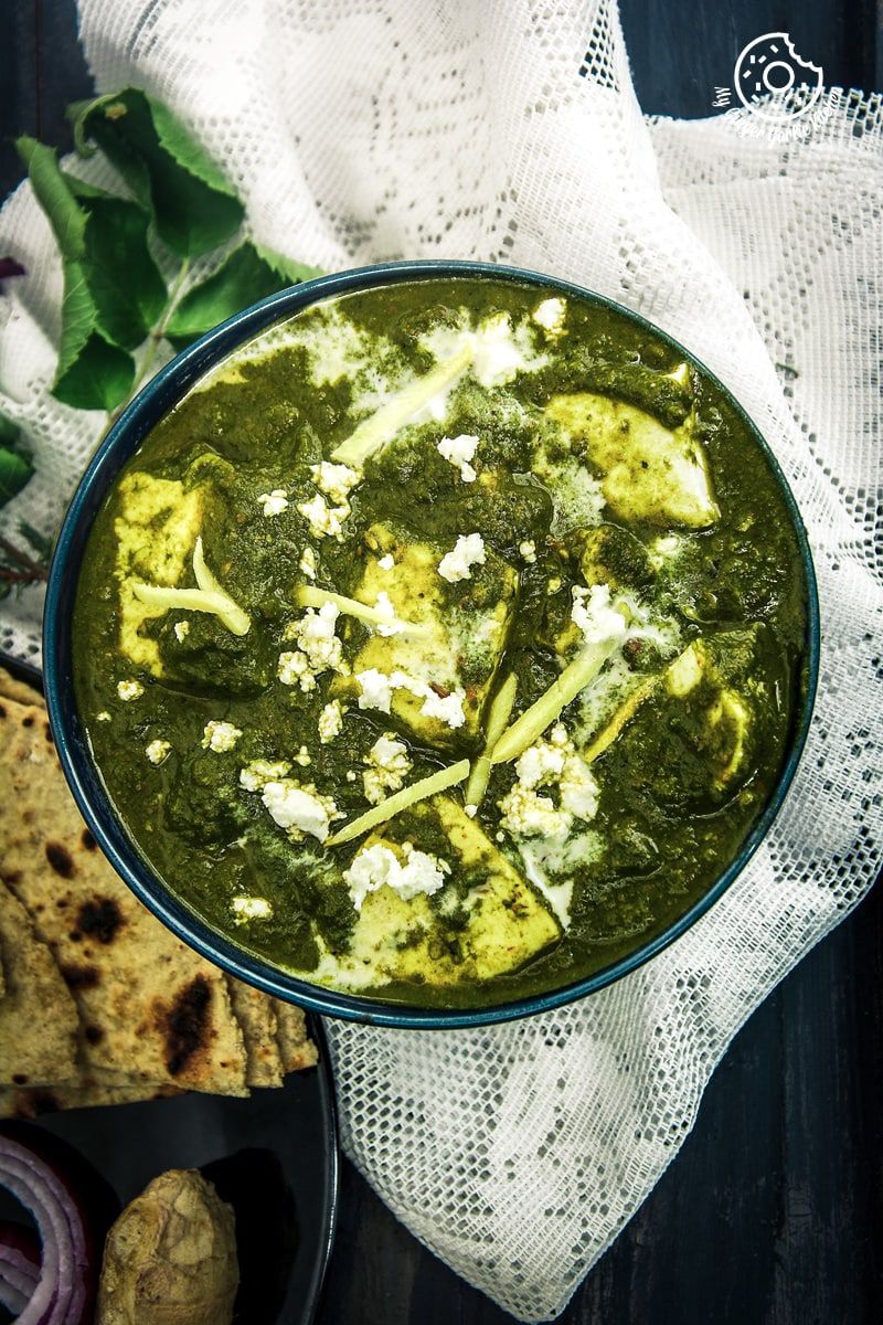 a bowl of palak paneer with some flatbreads on a white napkin