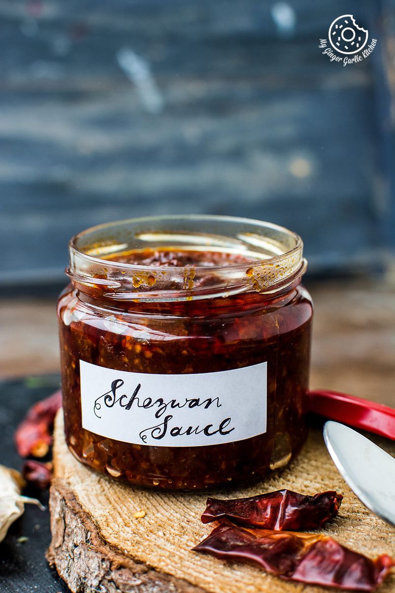 a jar of schezwan sauce on a wooden table with a spoon