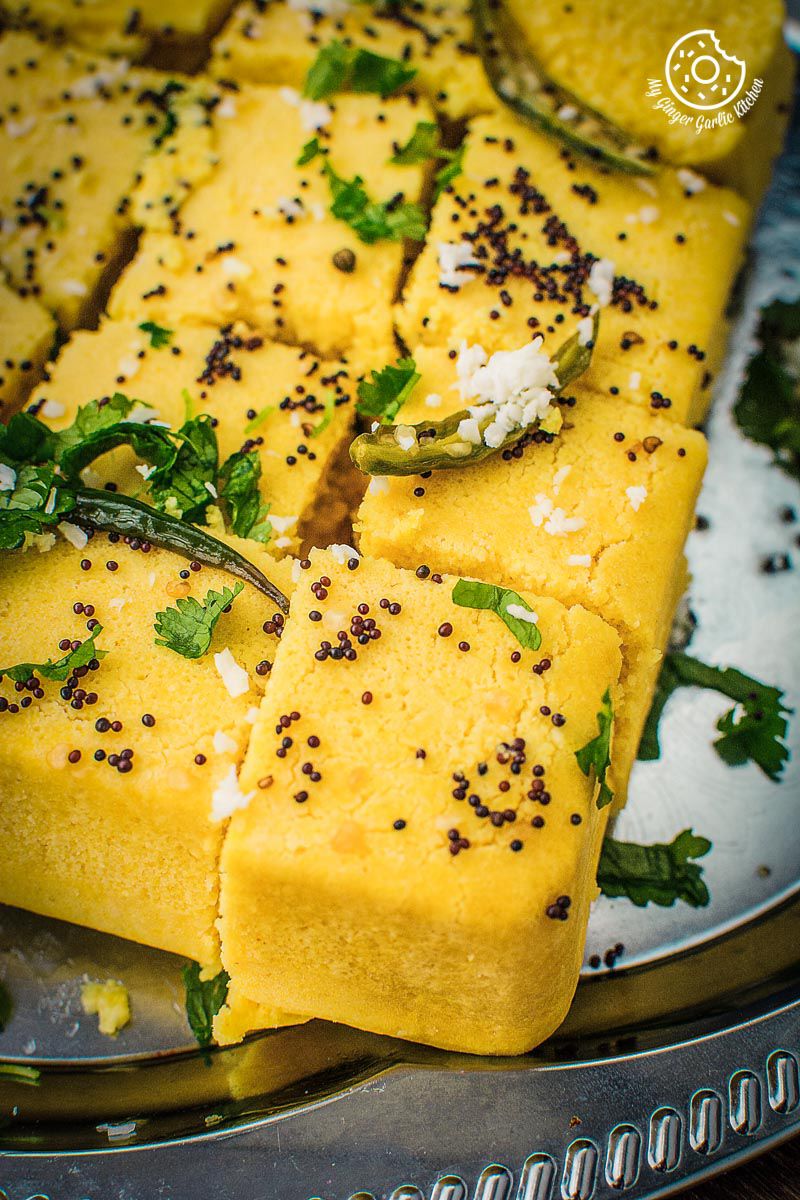 a plate of khaman dhokla topped with tempering and coconut