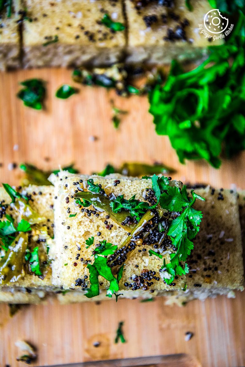 a stack of instant oats rava dhokla with herbs on it on a cutting board