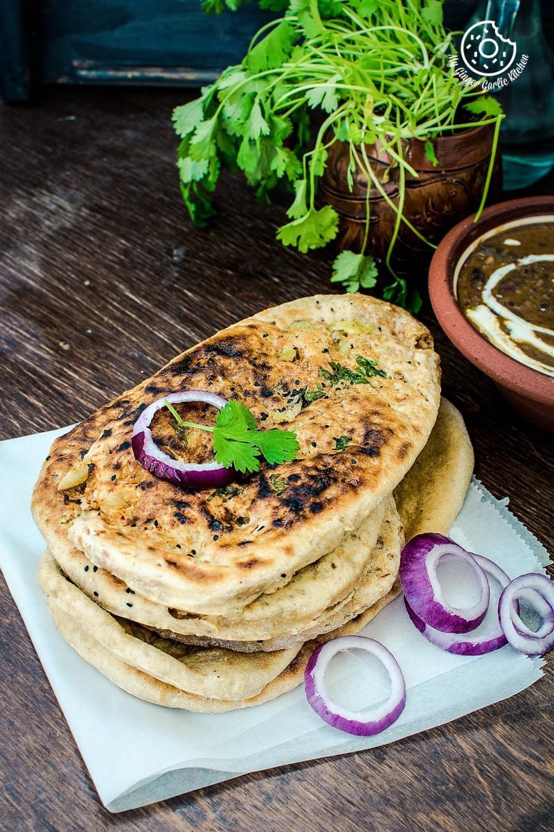 a stack of paneer stuffed naan with onions and herbs and a bowl of curry