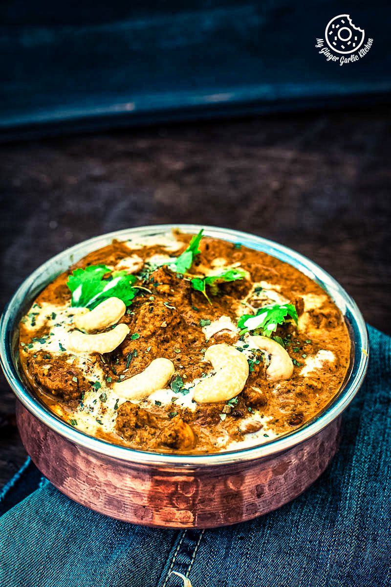 a bowl of restaurant style shahi kaju curry topped with cashews, cream and cilantro