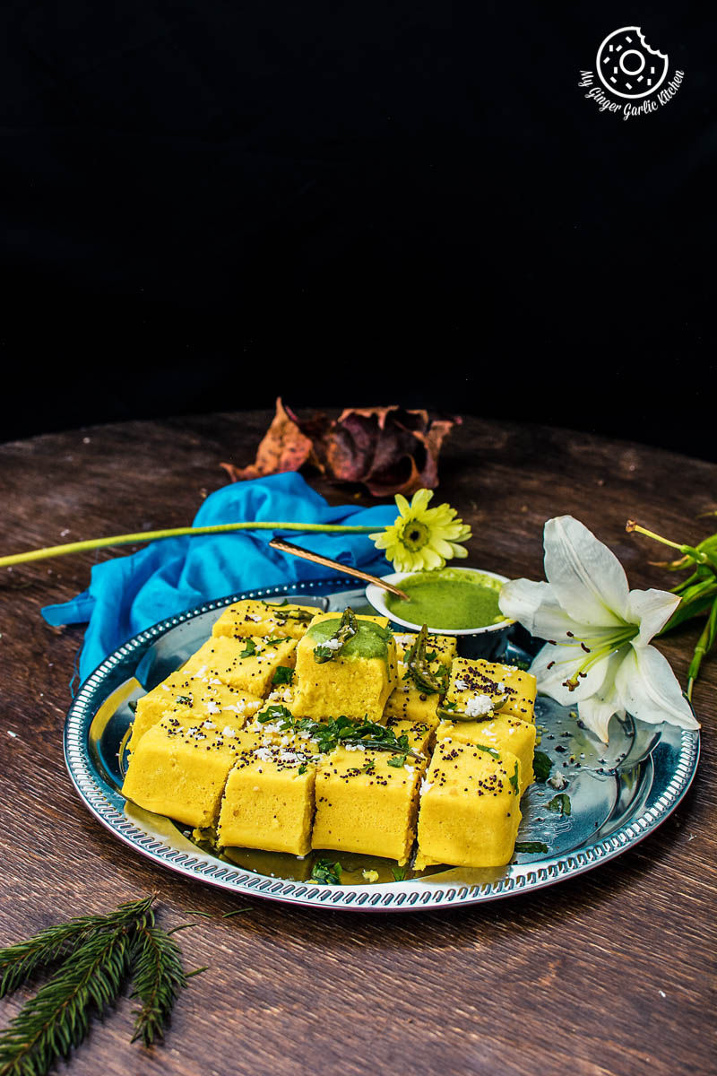 a plate of khaman dhokla with a bowl of green cilantro chutney on a wooden table