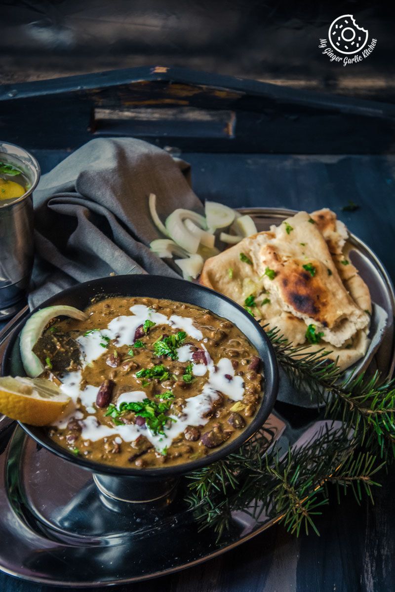 there is a bowl of Restaurant Style Dal Makhani and a plate of naan bread on a table