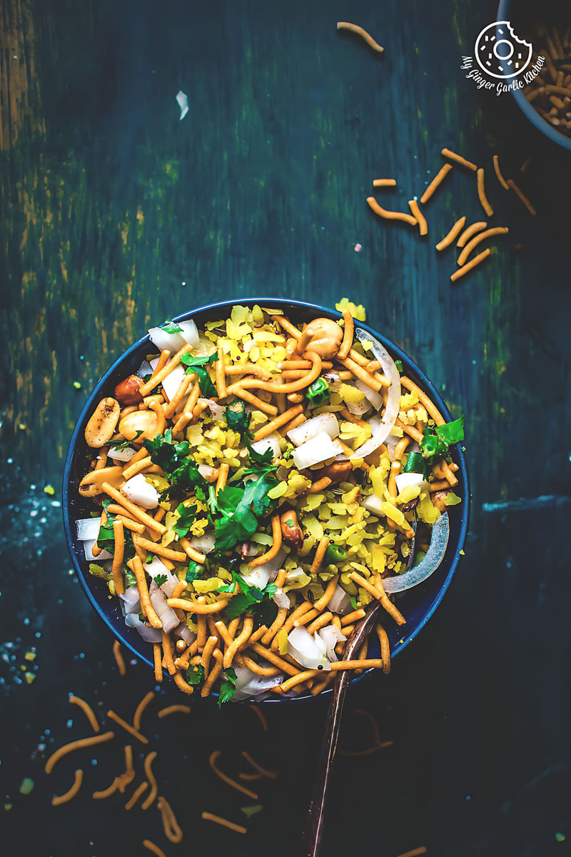 a bowl of khatta meetha indori poha with a topping of sev and cilantro on a table