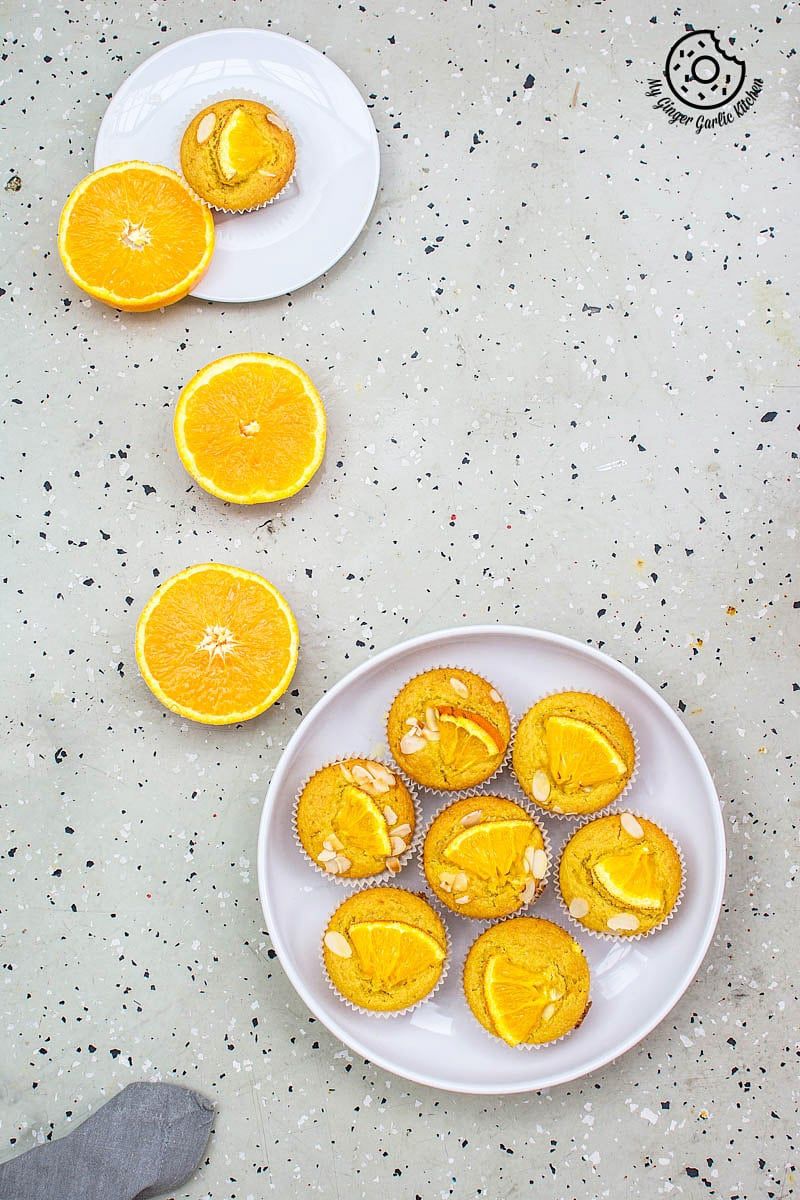 eggless orange olive oil muffins on a plate and some orange slices on a table