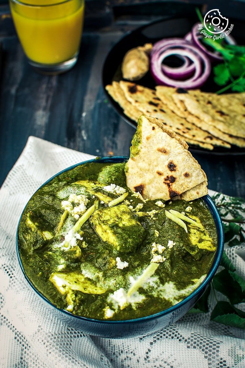 a bowl of palak paneer with some flatbreads, and a glass of orange juice