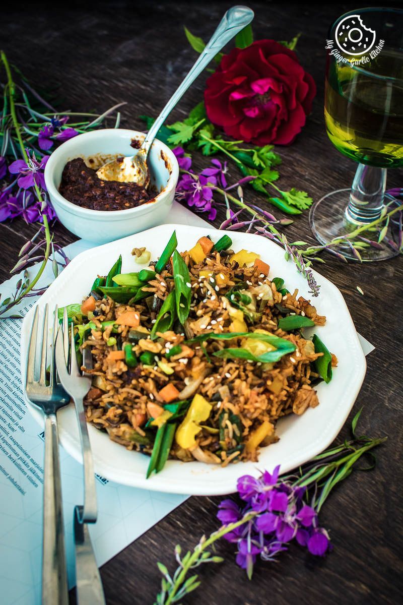 a plate of veg schezwan fried rice on a table with a glass of wine