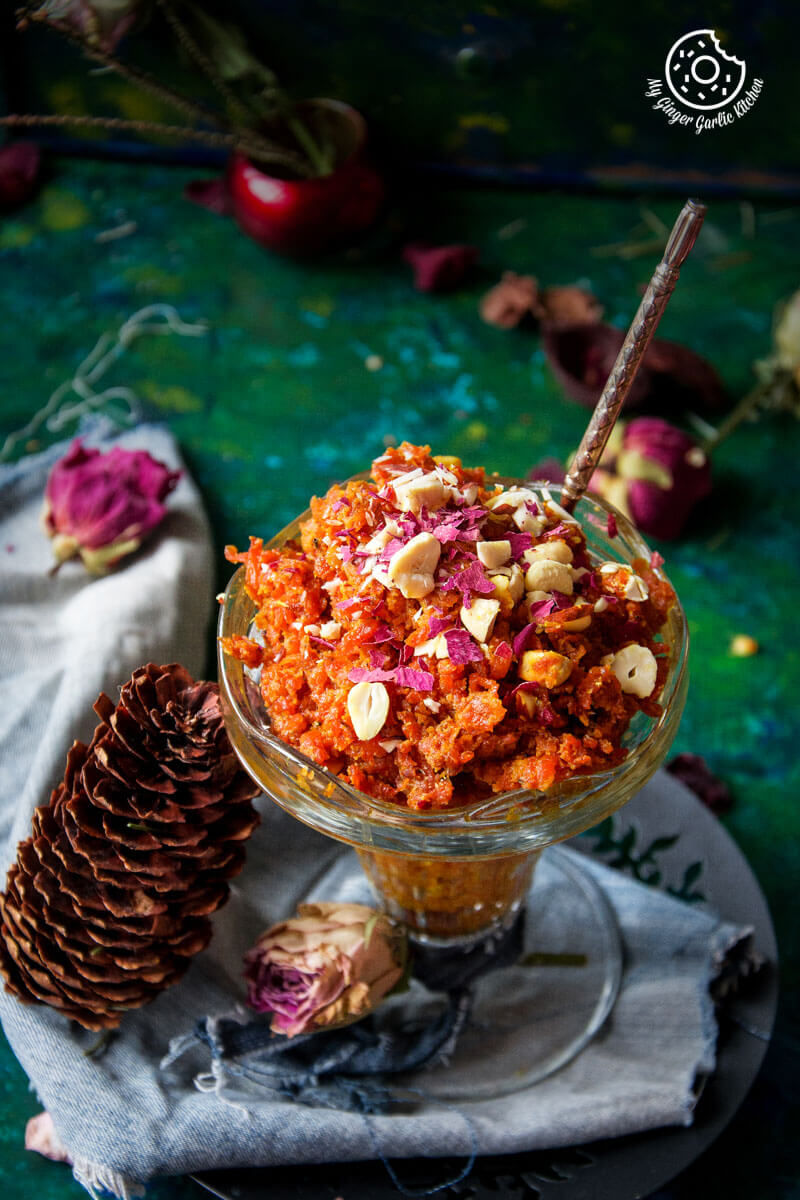 a bowl of gajar ka halwa topped with nuts a spoon and a pine cone