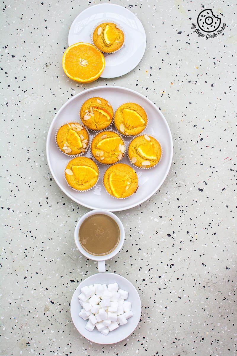 eggless orange olive oil muffins in a plate next to a cup of coffee and sugar