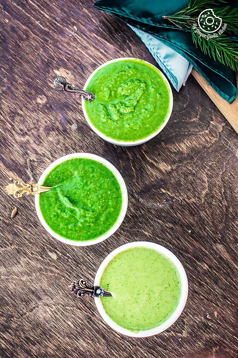 three bowls of green coriander chutney with a spoon in them