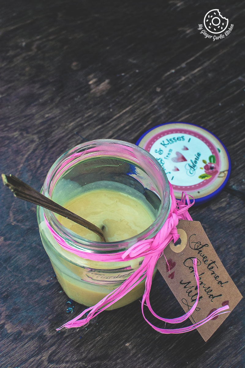 a jar of homemade sweetened condensed milk with a spoon in it