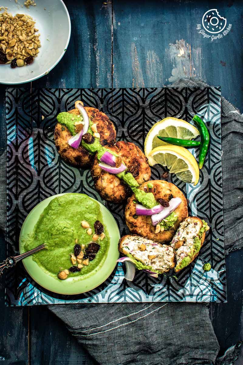 a close up of a plate of dahi ke kababs with a lemon slices and a bowl of green chutney