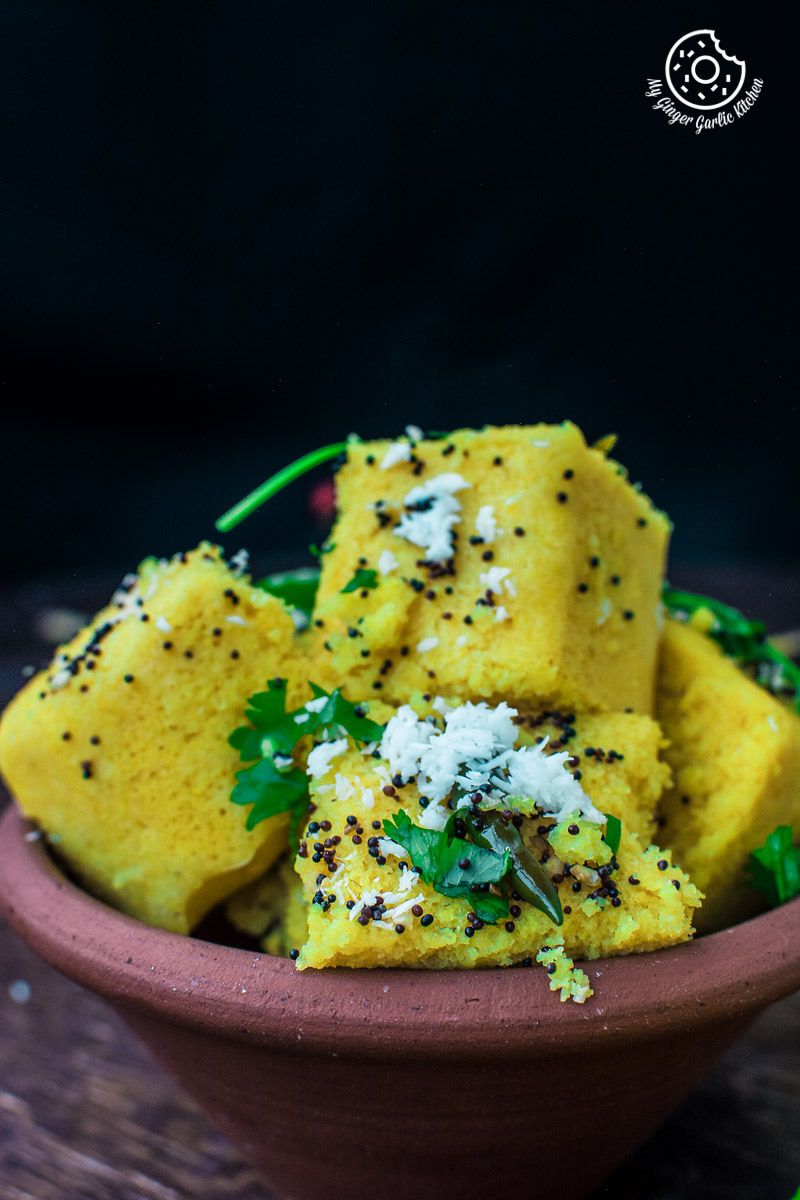 a bowl of soft and spongy khaman dhokla topped with tempering and fresh cilantro and coconut