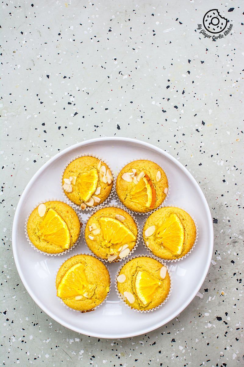 seven eggless orange olive oil muffins on a plate on a table