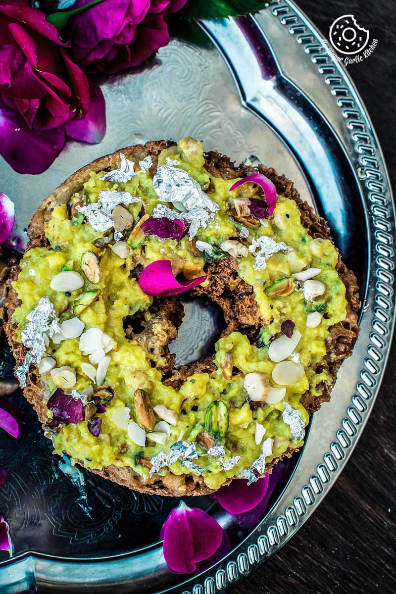 there is a plate with a rajasthani ghevar covered in rabri, nuts and flowers