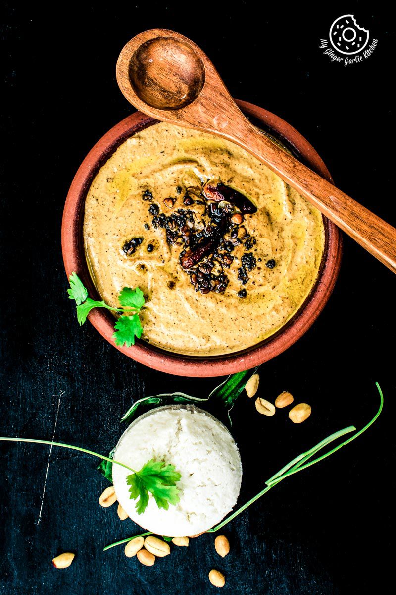 a bowl of south indian style peanut garlic chutney with a spoon and some herb and goan sanna