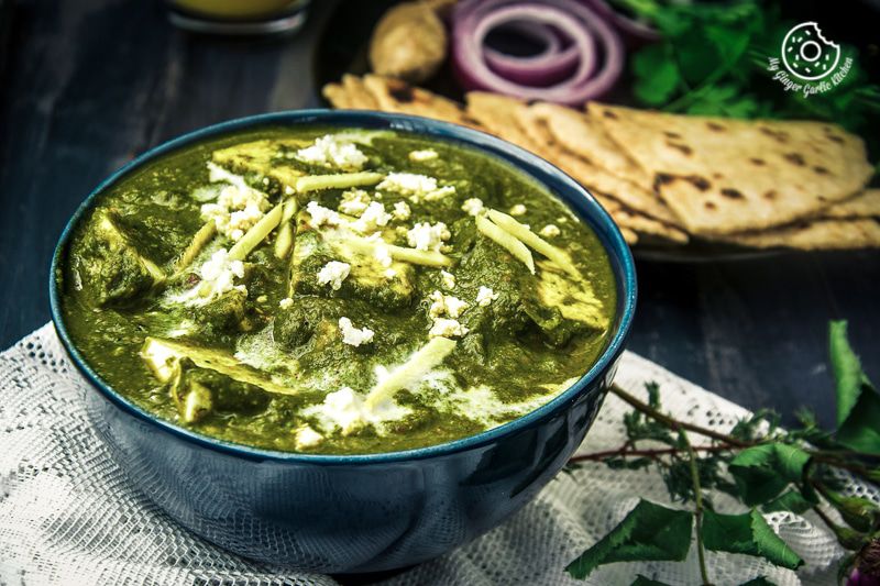 a bowl of palak paneer with some flatbreads on a table
