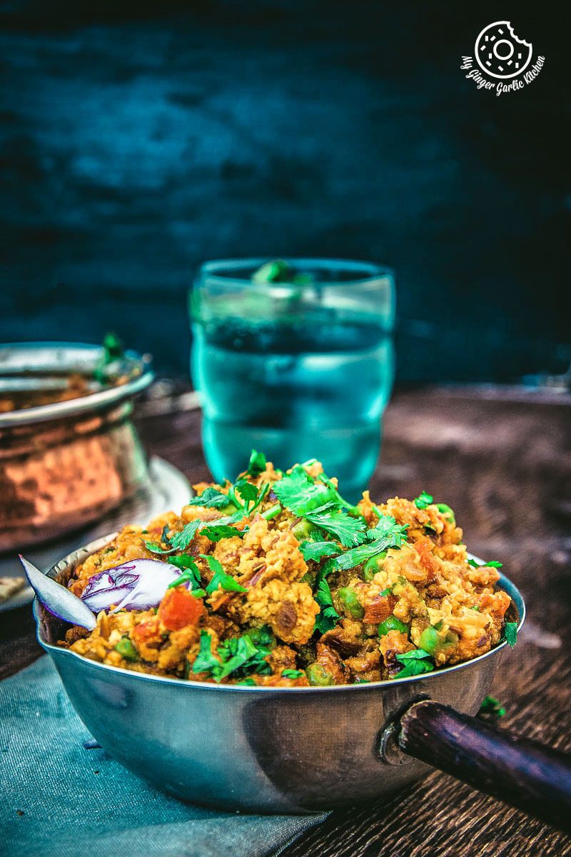 a bowl of punjabi paneer bhurji dry with a spoon and a glass of water