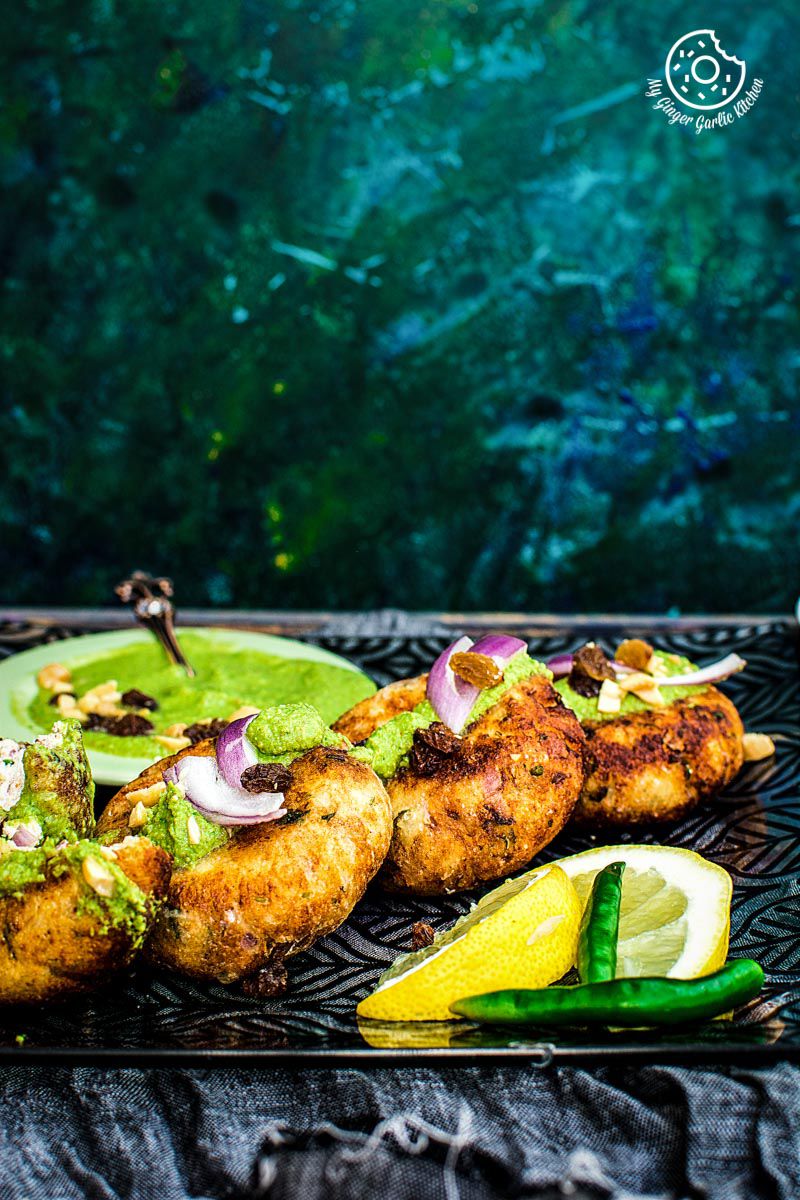 a plate of dahi ke kabab with a side of chutney with green chilies and lemon slices