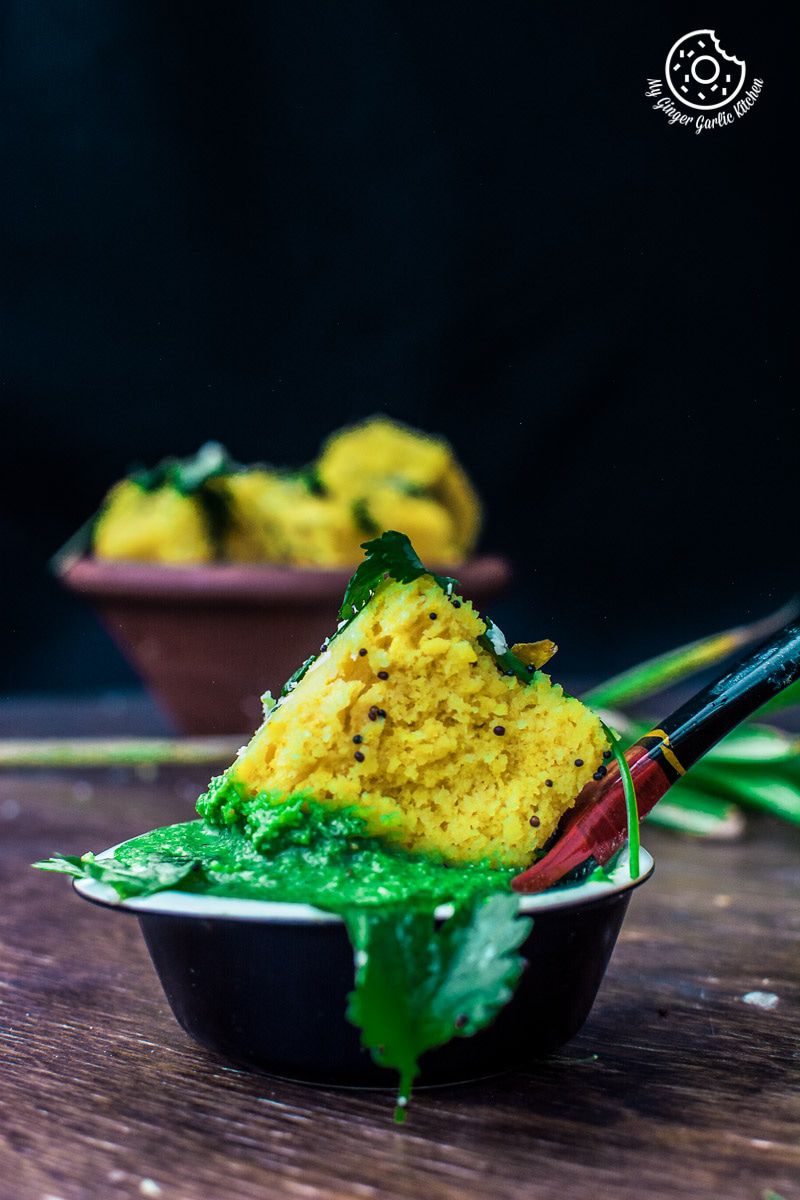 a soft khaman dhokla dunked in a bowl of green coriander chutney
