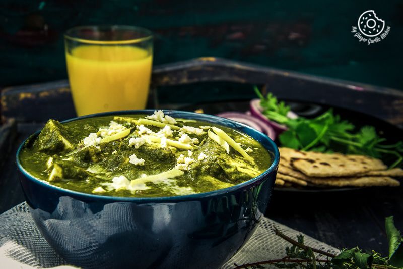 a bowl of palak paneer with some flatbreads on a table