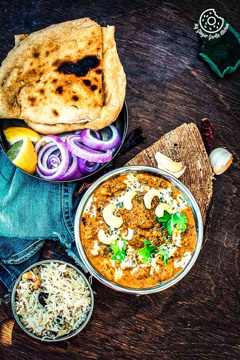 bowl of restaurant style shahi kaju curry with some naan, pulao and salad