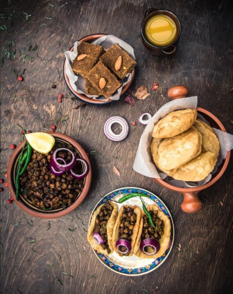 overhead view of a table with plates of halwa chana poori ashtami prashad and a glass of orange juice