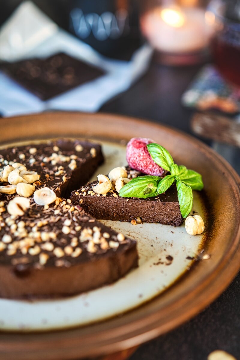 Slice of vegan chocolate banana cake with hazelnuts and basil on a ceramic plate