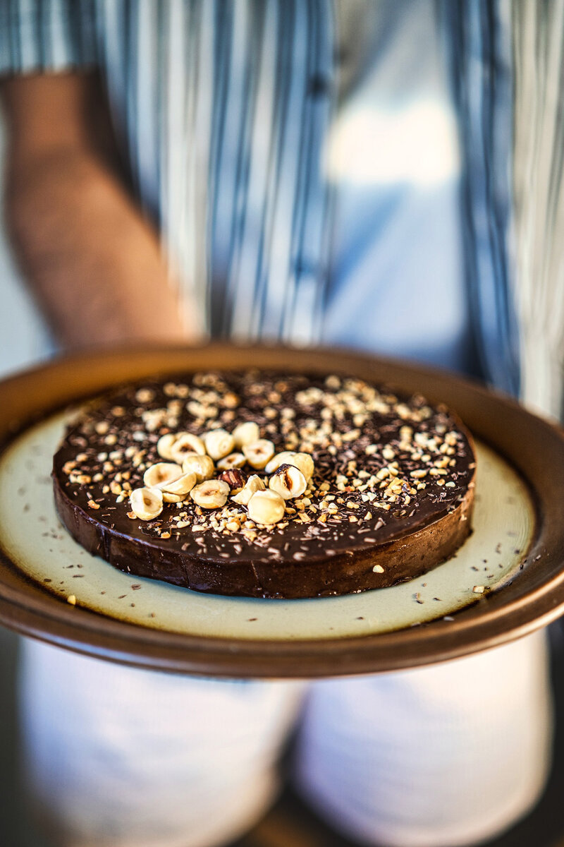 Person holding homemade chocolate banana cake topped with crunchy hazelnuts