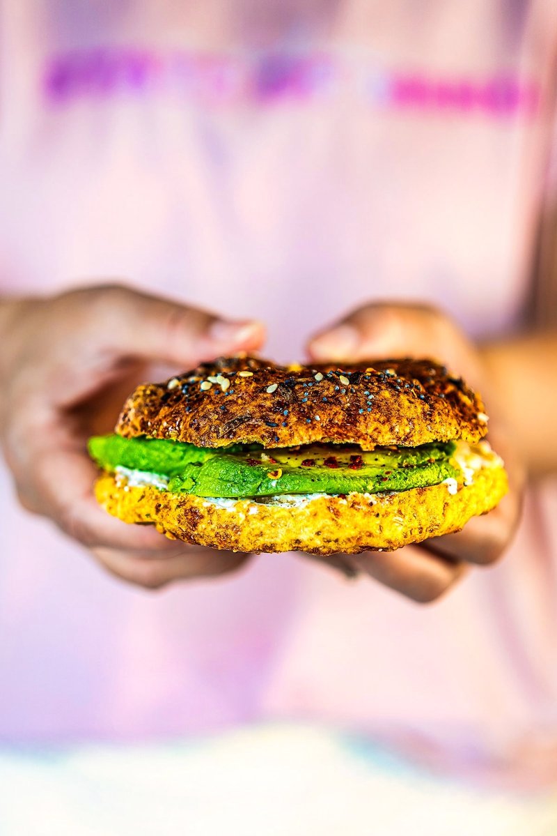 Hands holding a high protein cottage cheese bagel sandwich with cream cheese and avocado slices.