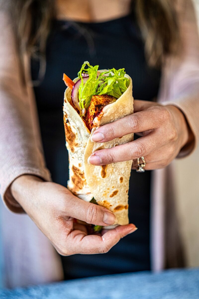 hand holding a soft cottage cheese tortilla wrap filled with tofu, lettuce, and vegetables