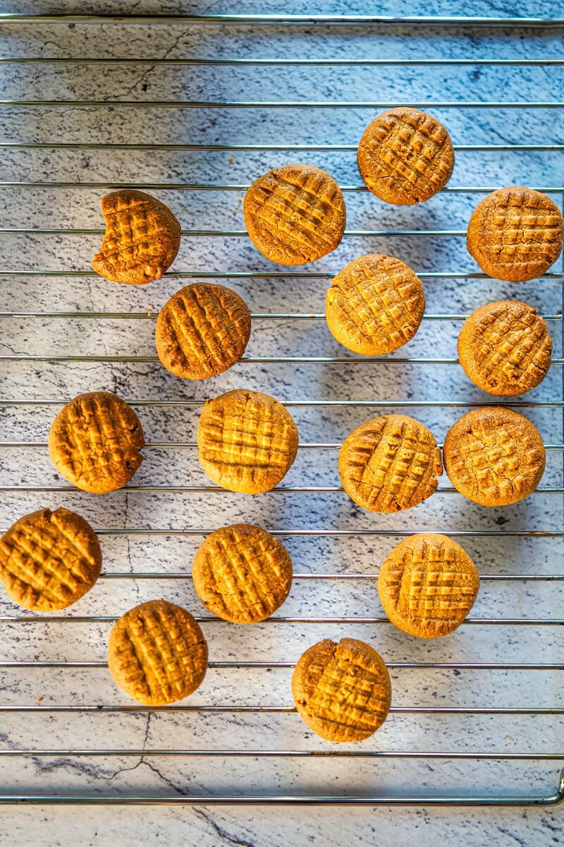 Fresh homemade 2-ingredient peanut butter cookies cooling on wire rack with crisscross tops and one bitten cookie
