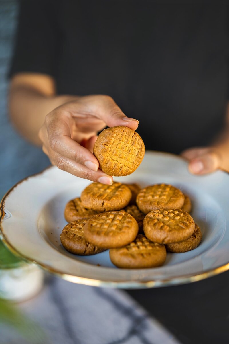Hand holding a golden 2-ingredient peanut butter cookie above plate, showing simple homemade recipe cookies
