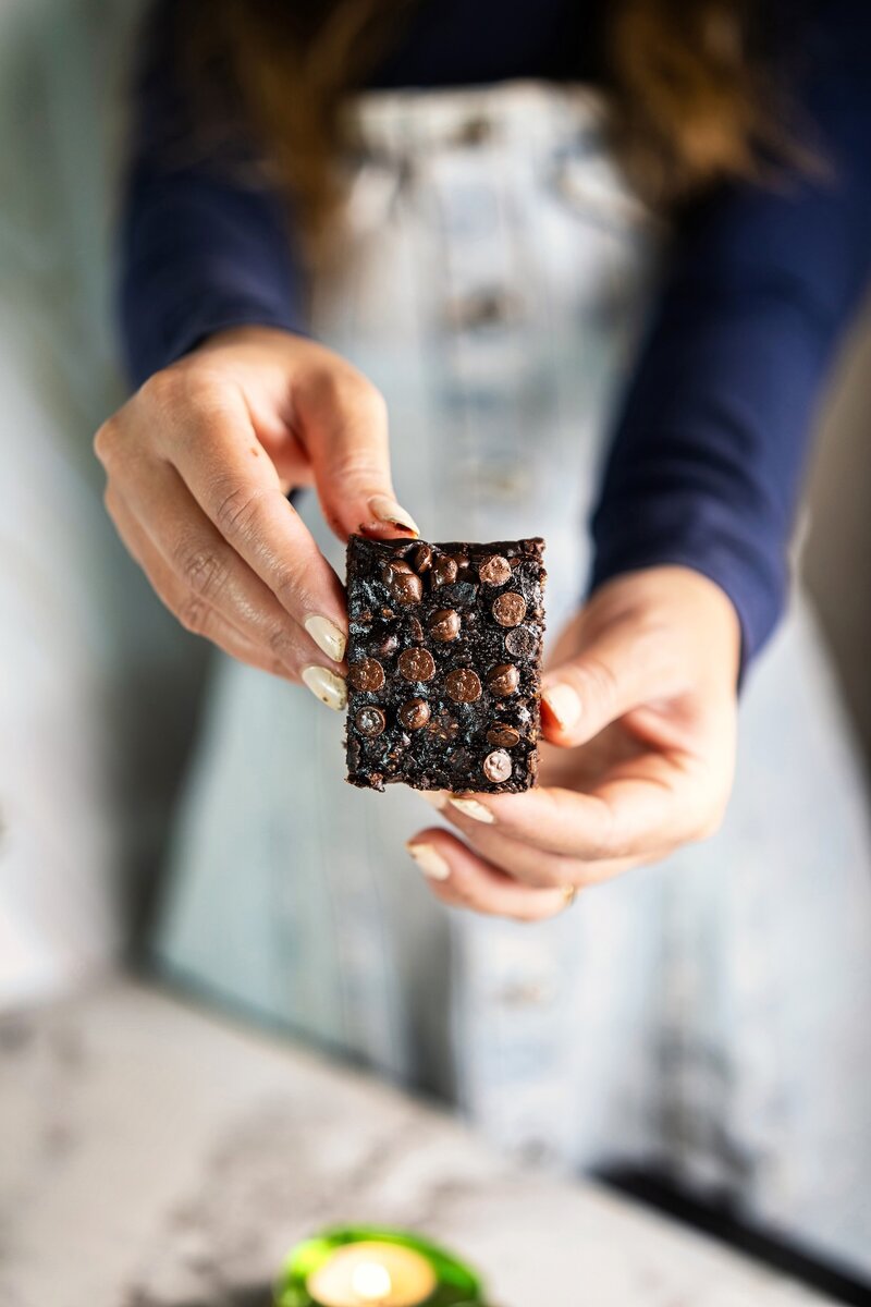 Hand holding a square of 3-ingredient banana peanut butter brownie with melted chocolate chips