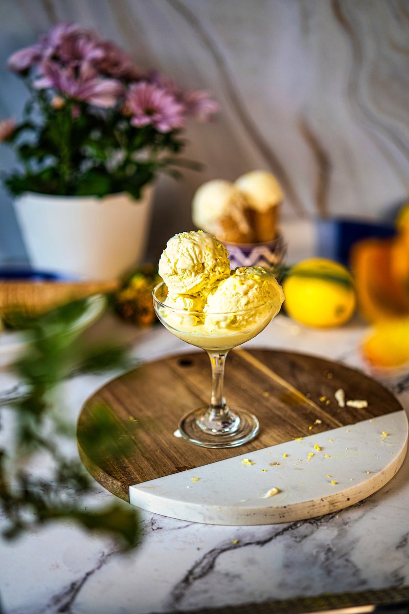 Homemade no churn lemon ice cream in a glass dessert bowl on a wooden serving board with fresh lemons in the background.