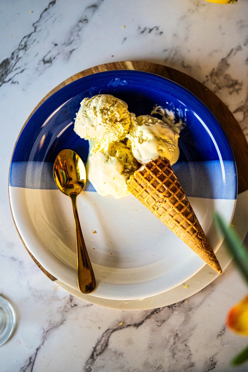 Overhead view of homemade lemon ice cream scoops with a waffle cone and gold spoon on a blue plate.