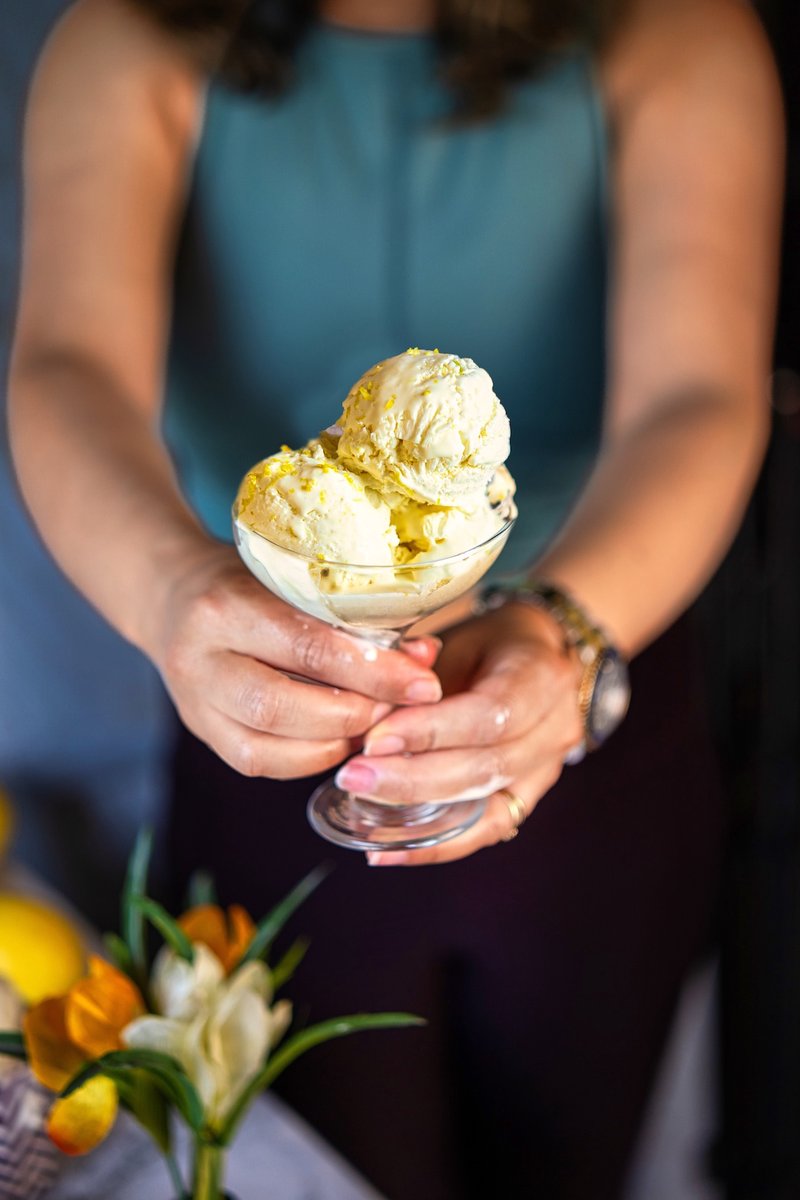 Hands holding a glass bowl filled with creamy homemade no churn lemon ice cream topped with fresh lemon zest.