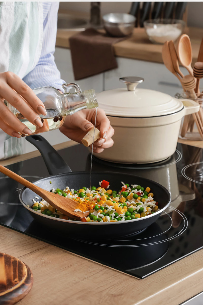 Person pouring oil into a skillet filled with mixed vegetables.