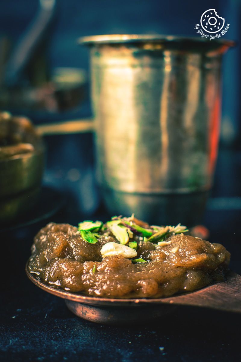 a plate of aata ka halwa on a table with a glass in the background