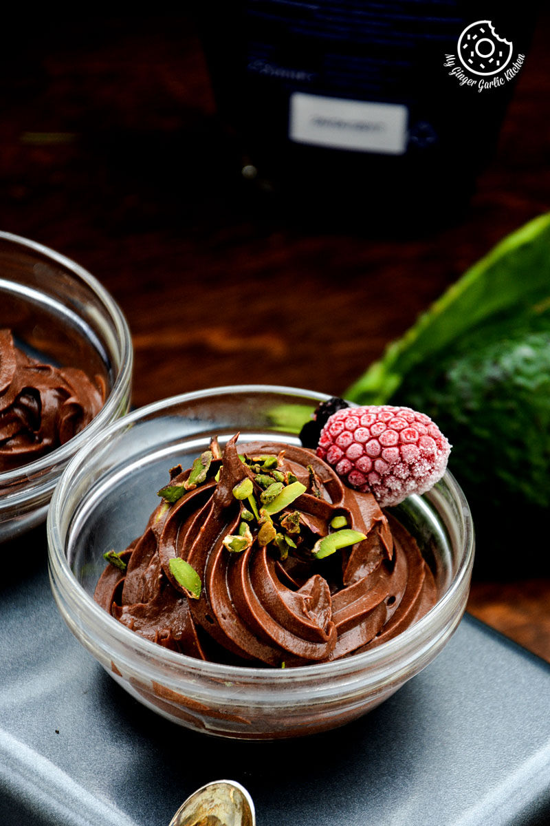 two bowls of avocado chocolate mousse with a raspberry on top