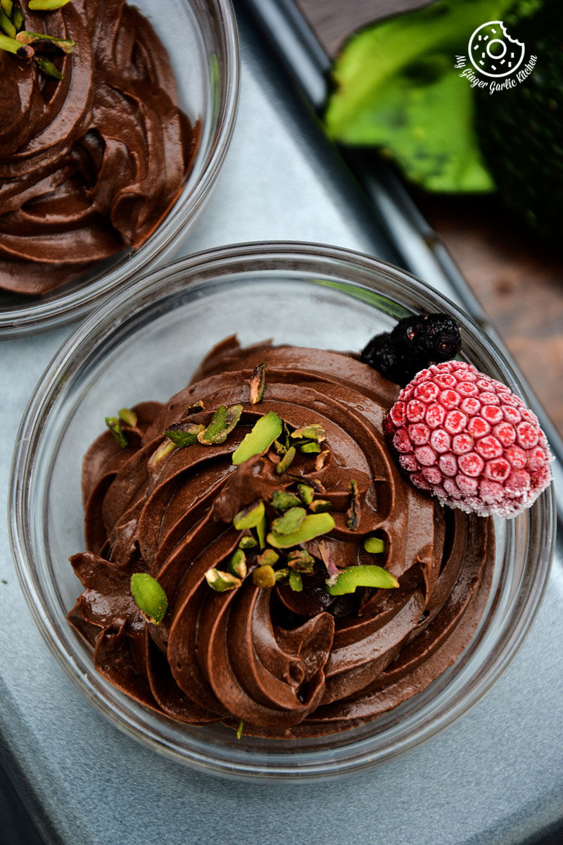 two bowls of avocado chocolate mousse with raspberries and pista