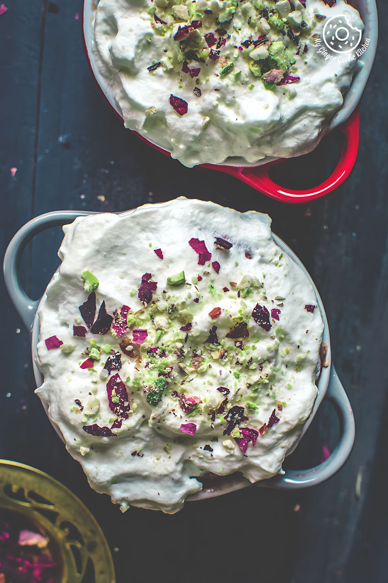 two bowls of eggless gulknad mug cake with whipped cream frosting and flowers on a table