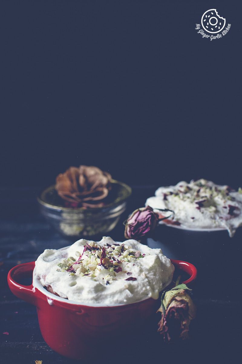a red mini casserole dish filled with eggless gulknad mug cake with whipped cream and flowers